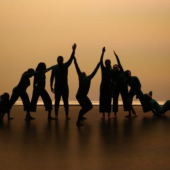 Silhouetted group dance performance with dancers in dynamic poses.